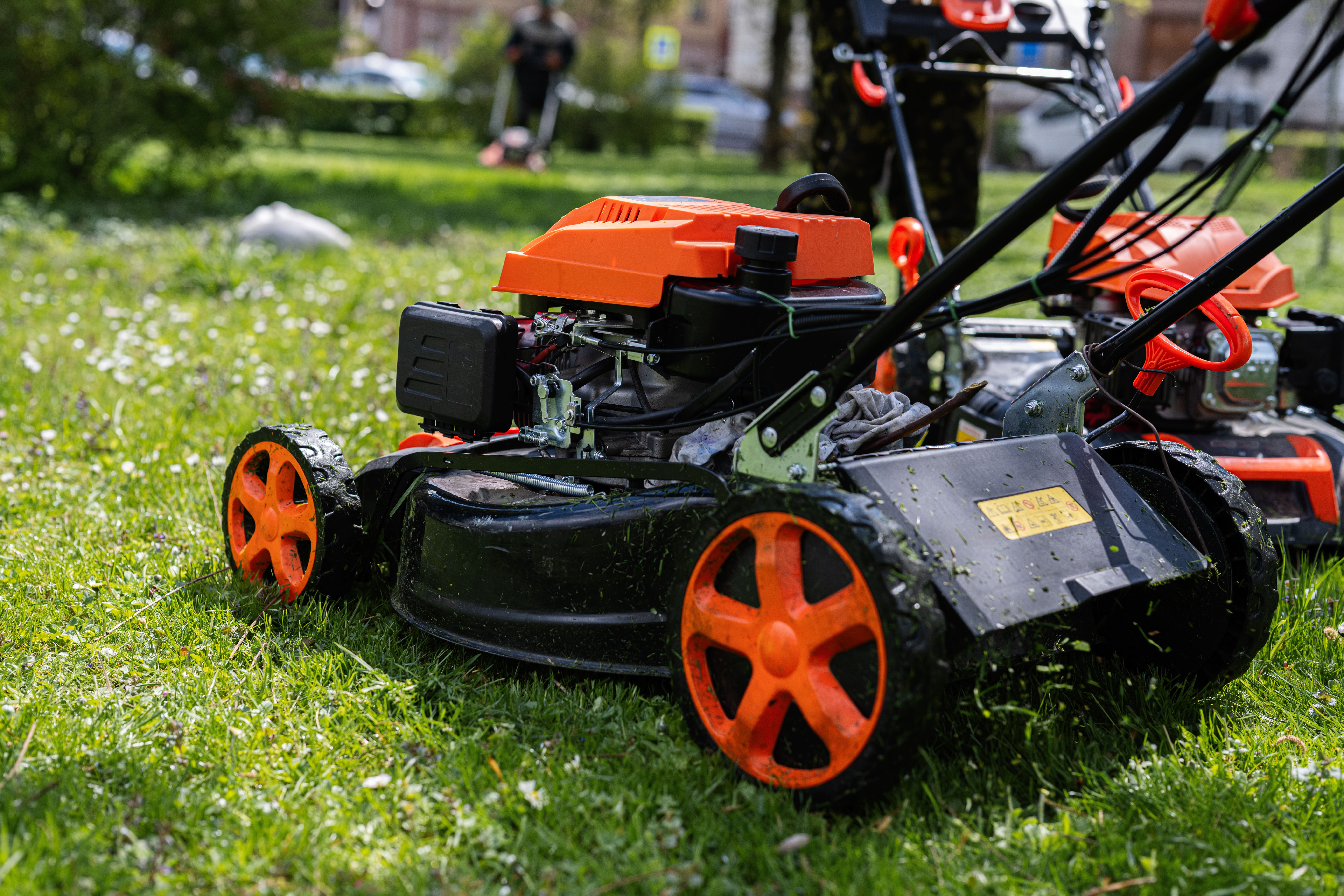 A photograph of a gardener or communal services worker, a man, using a lawn mower to cut the grass in a city park or urban green space